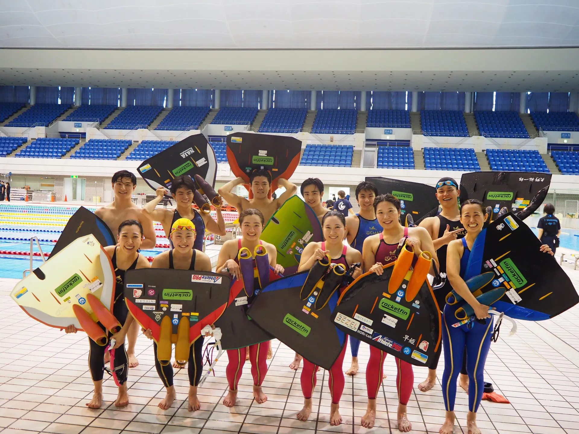 フィンスイミング選手たちがモノフィンを持ちプールサイドで集合写真