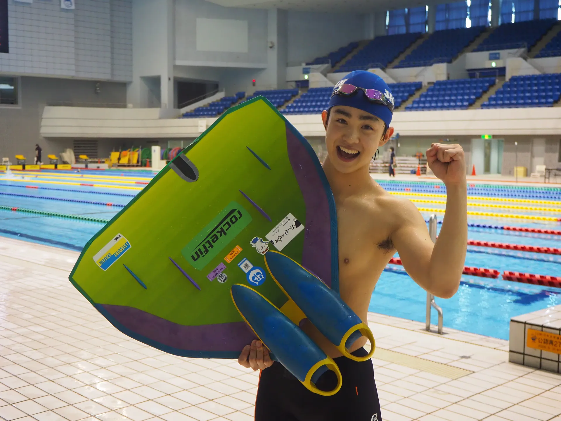 100mサーフィスにてフィンスイミングユース日本新記録を樹立した稲毛眞生選手がモノフィンを持ち競泳プールの前で笑顔でポーズ