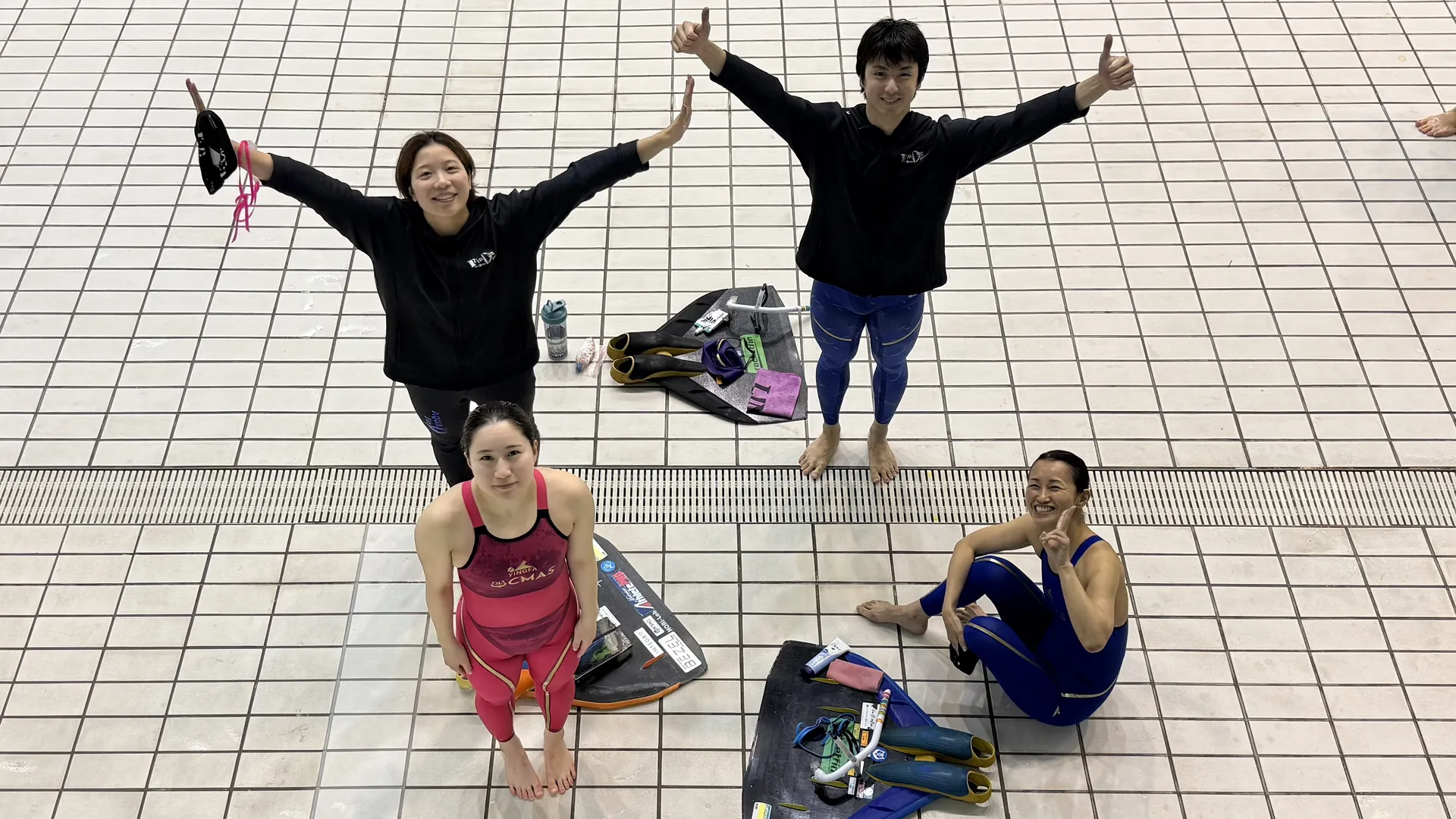 AQUA FinDのメンバー4人がプールサイドでフィンを持ち笑顔でポーズ