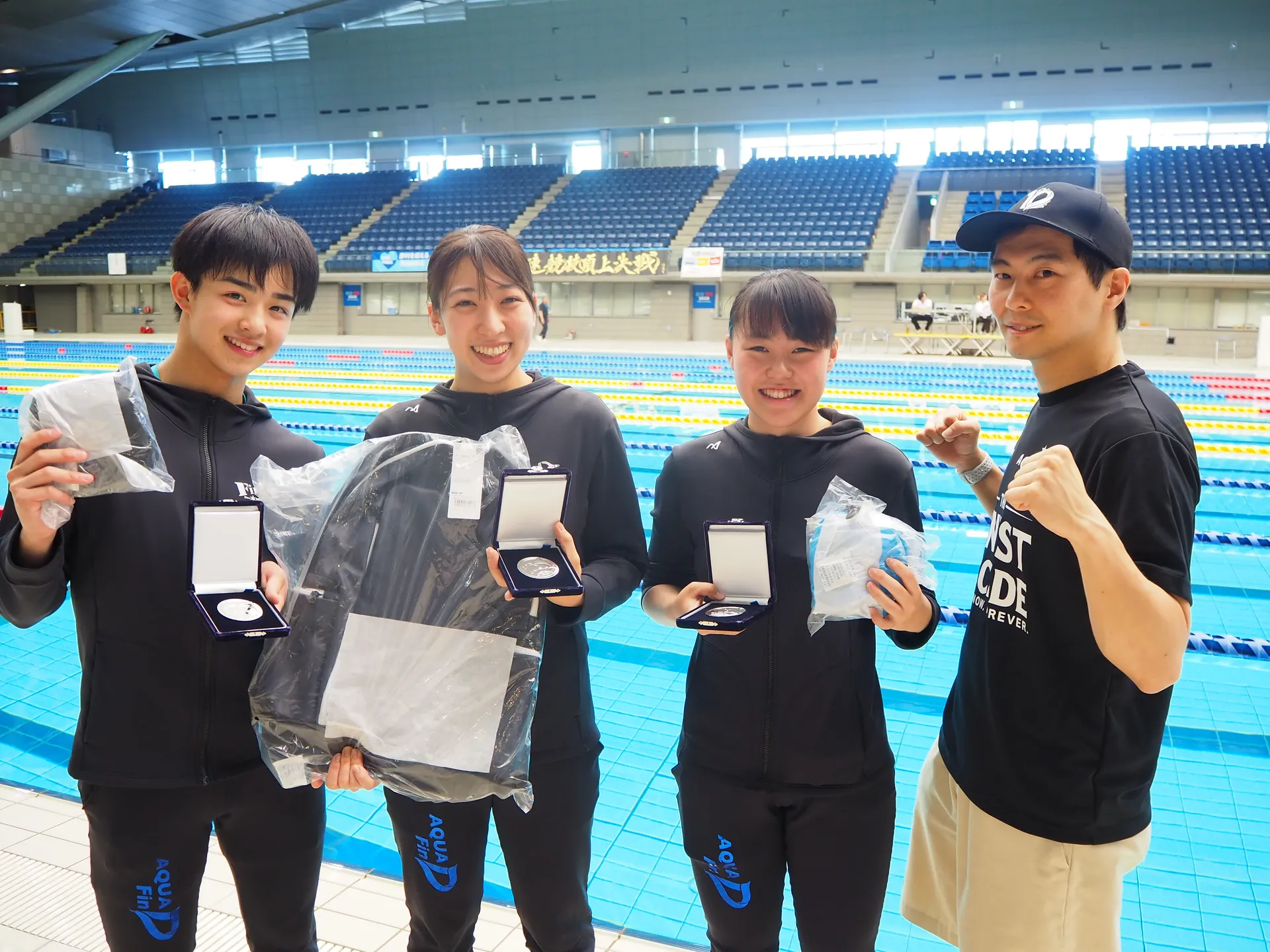 AQUA FinDの選手4名がプールサイドでメダルと賞品を掲げて笑顔で記念撮影
