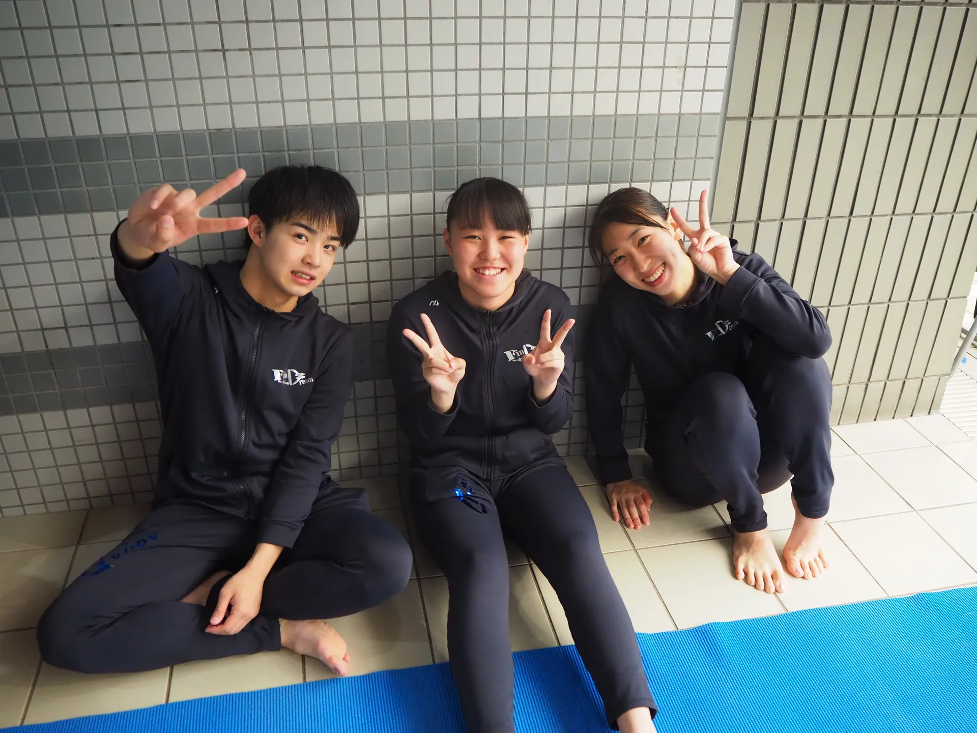 AQUA FinDのフィンスイミング選手3名がプールサイドでピースサインで笑顔の記念写真