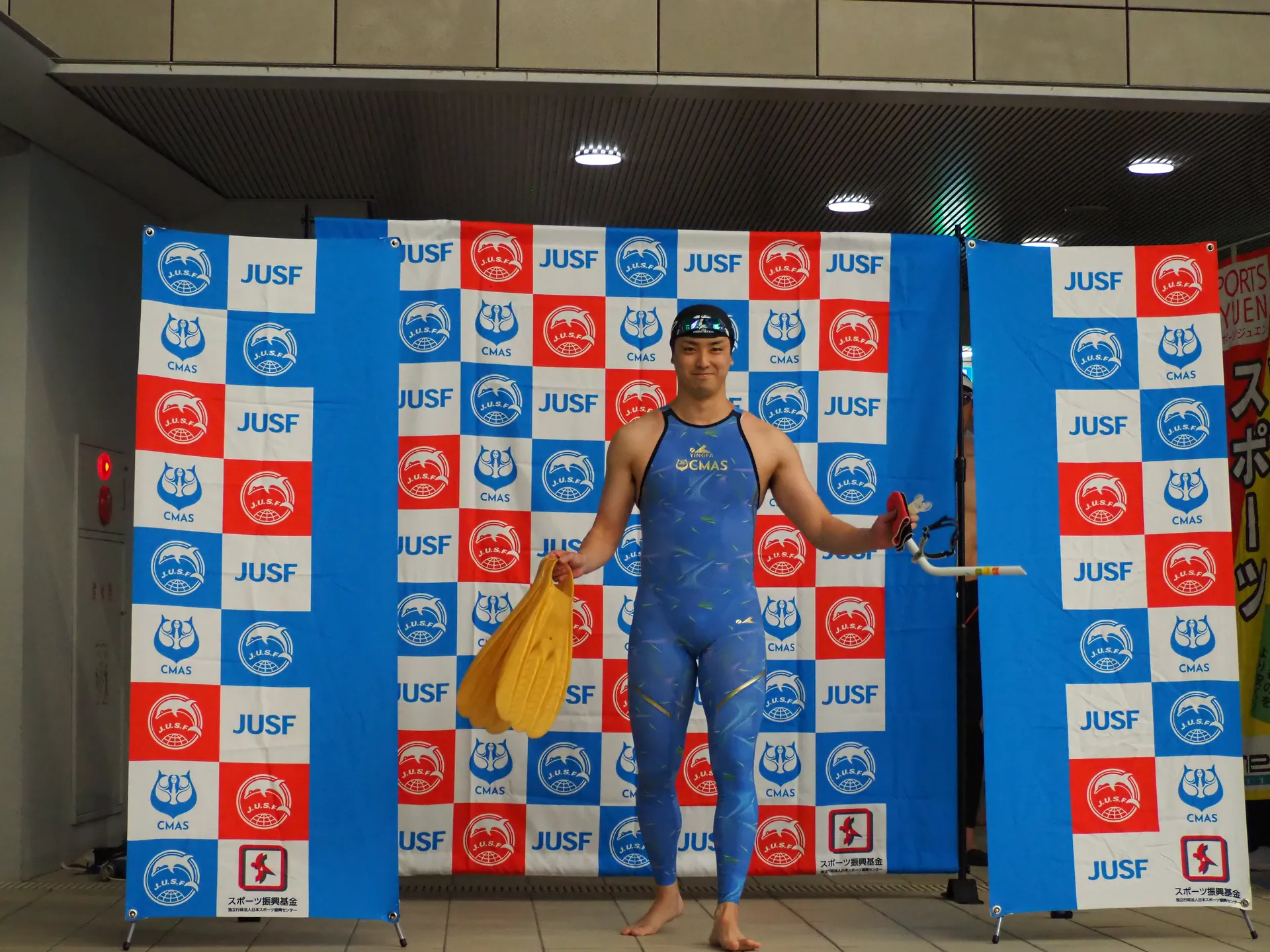 JUSF・CMAS公式バックパネル前でフィンを持つフィンスイミング選手