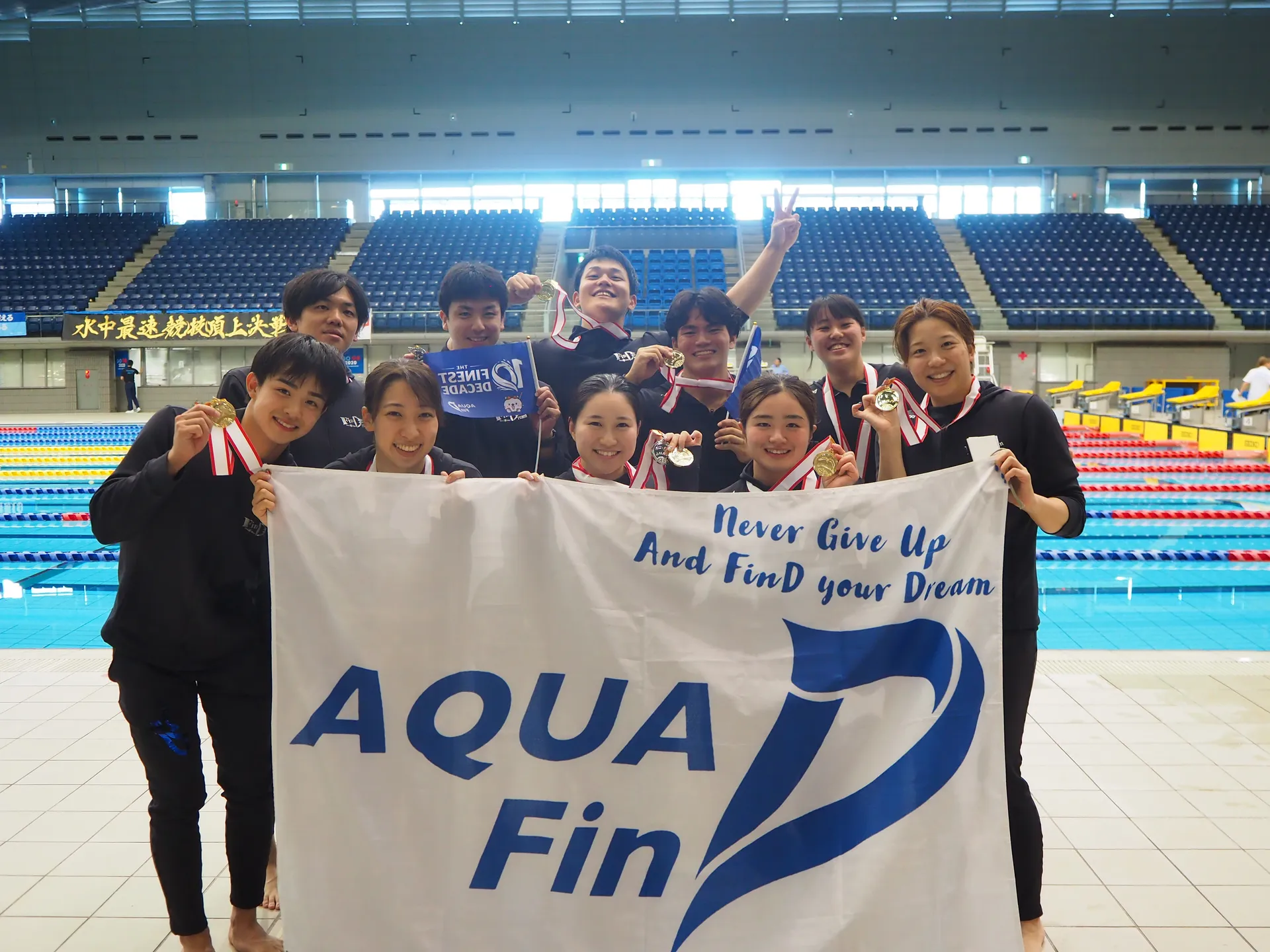 AQUA FinDのメンバーがメダルとチーム旗を掲げて記念撮影するフィンスイミング大会の集合写真
