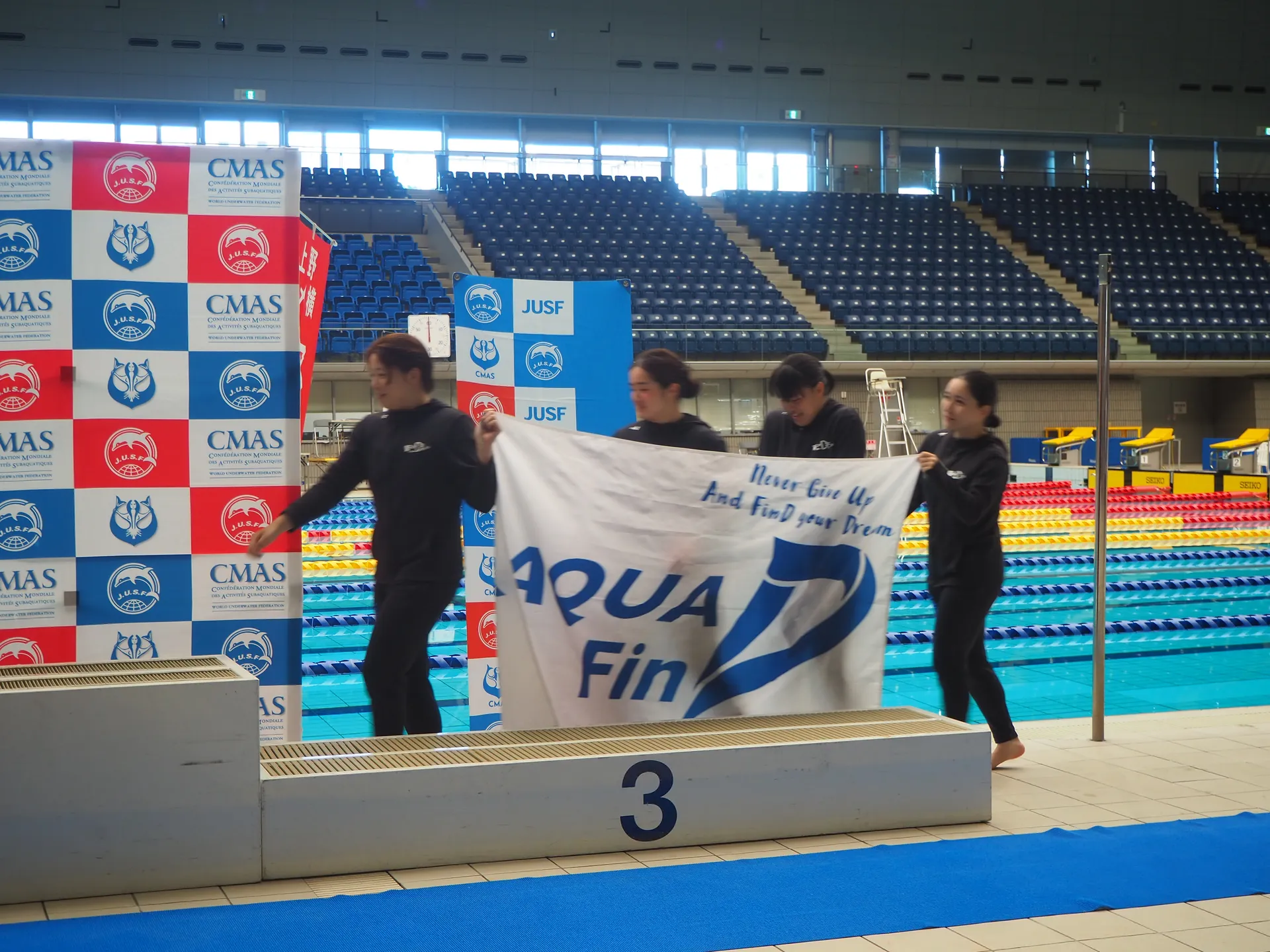 AQUA FinDのメンバーがCMAS・JUSF公式大会プールサイドでチーム旗を掲げる記念写真